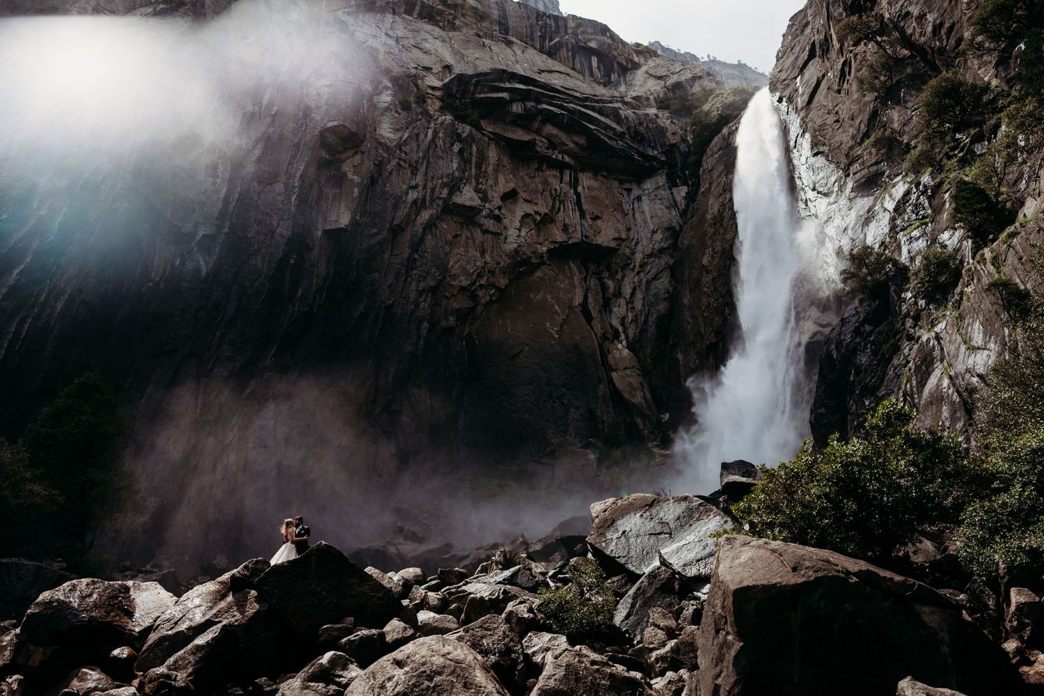 Wedding couple posing near misty waterfall on rocky mountain terrain. Yosemite national Park California.