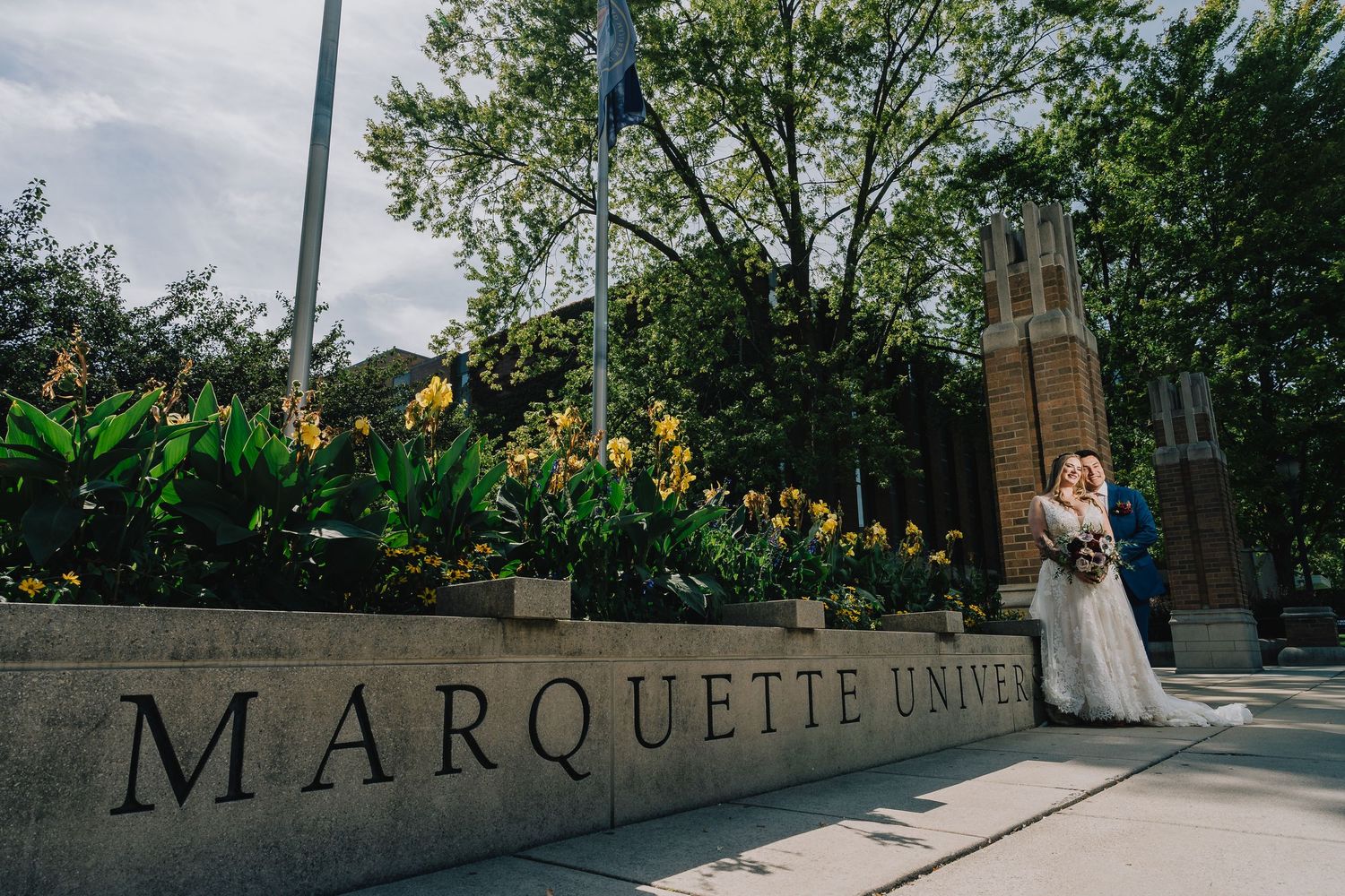 A couple poses for wedding photos at Marquette University with flowers and architecture in the background. Milwaukee