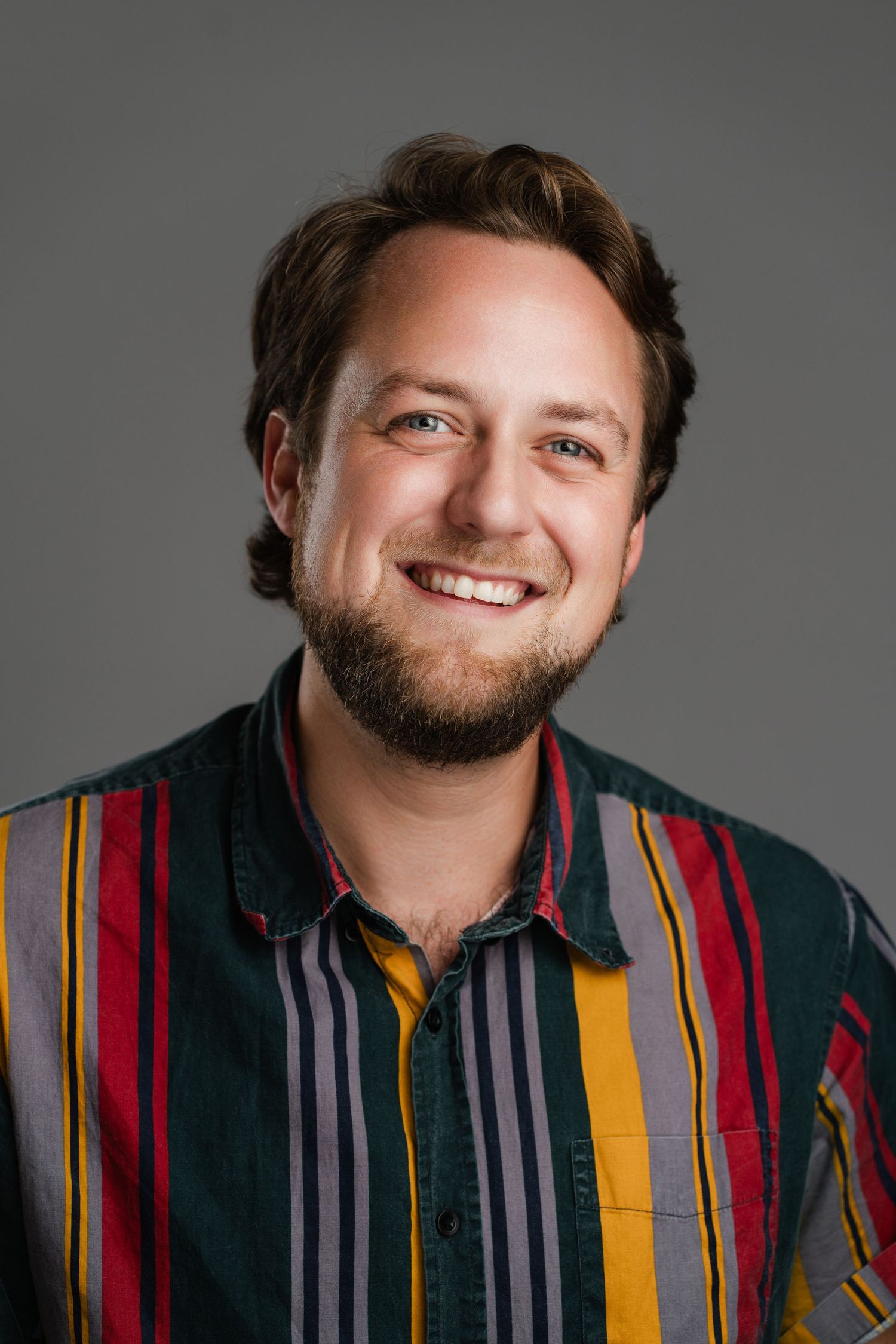 Portrait of someone wearing colorful striped shirt with warm smile against dark background. Nashville, Tennessee.