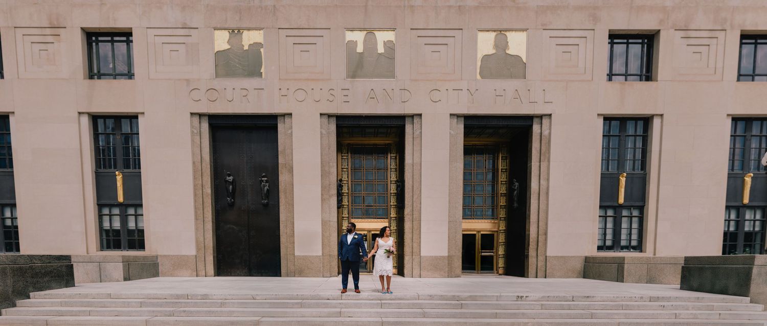 Wide architectural shot of a couple posing in front of a grand pink building entrance. Nashville, Tennessee courthouse.