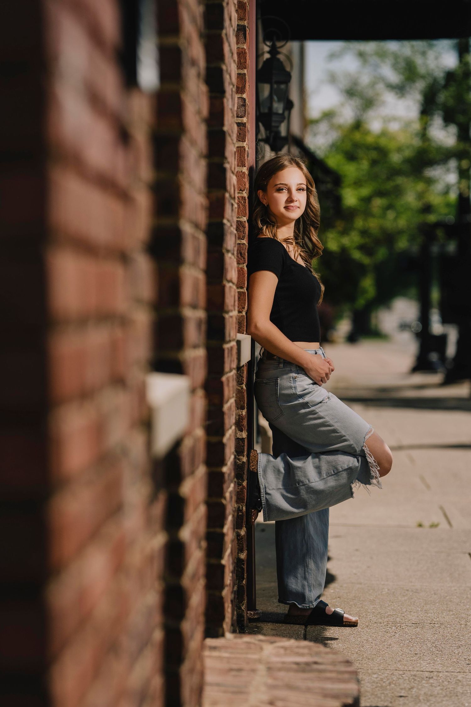 An artistic portrait of someone leaning against a brick wall in casual attire on a sunny day. Murfreesboro, Tennessee.