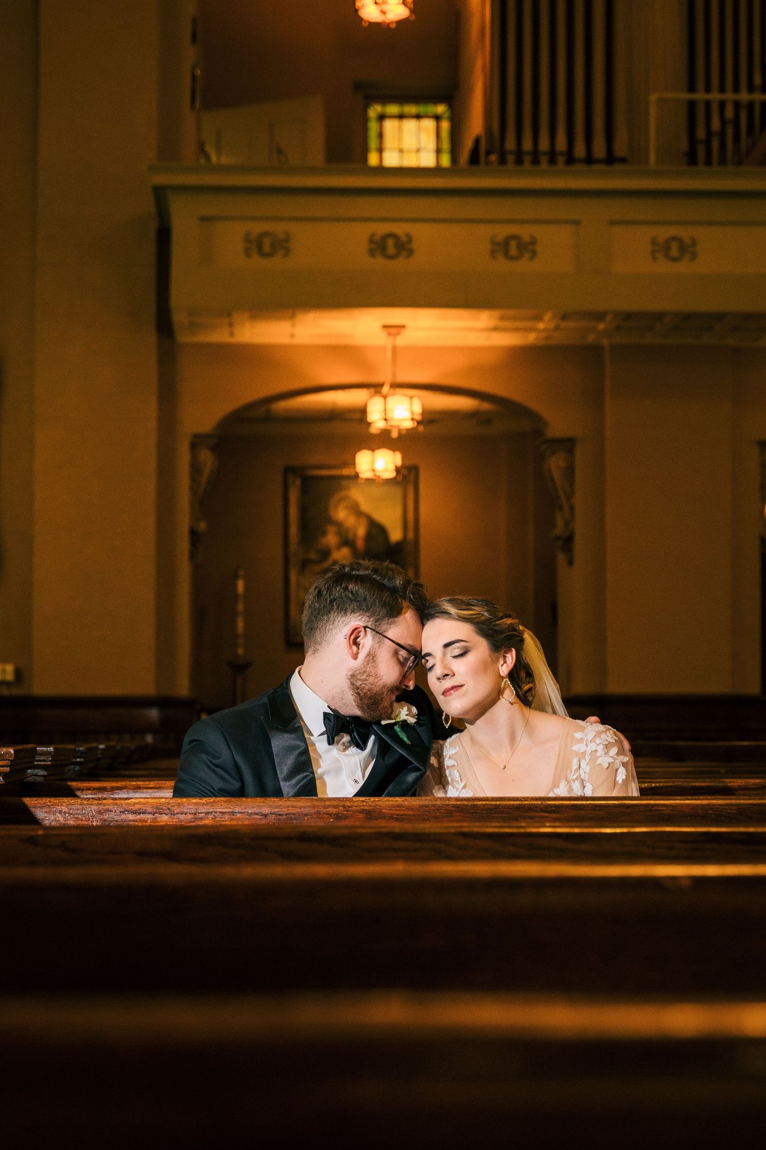 Couple shares tender moment in church pew under warm lighting. Nashville, Tennessee, Catholic Church.