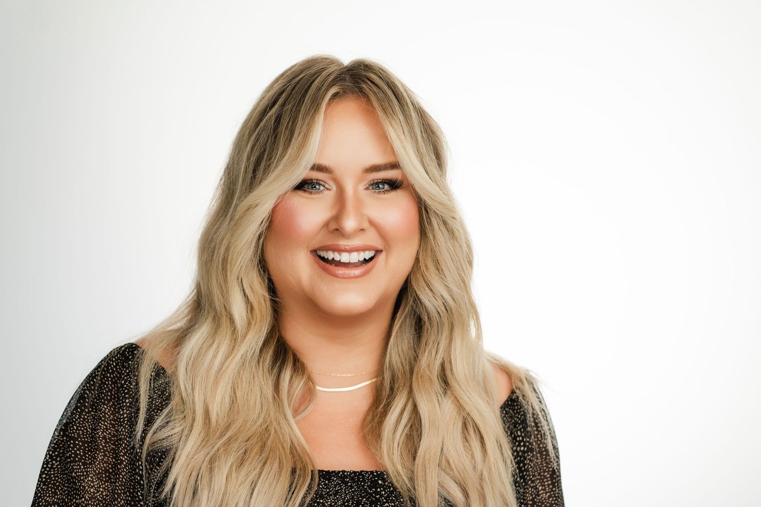 Portrait of woman with long blonde wavy hair wearing black top against white background. Nashville, Tennessee.