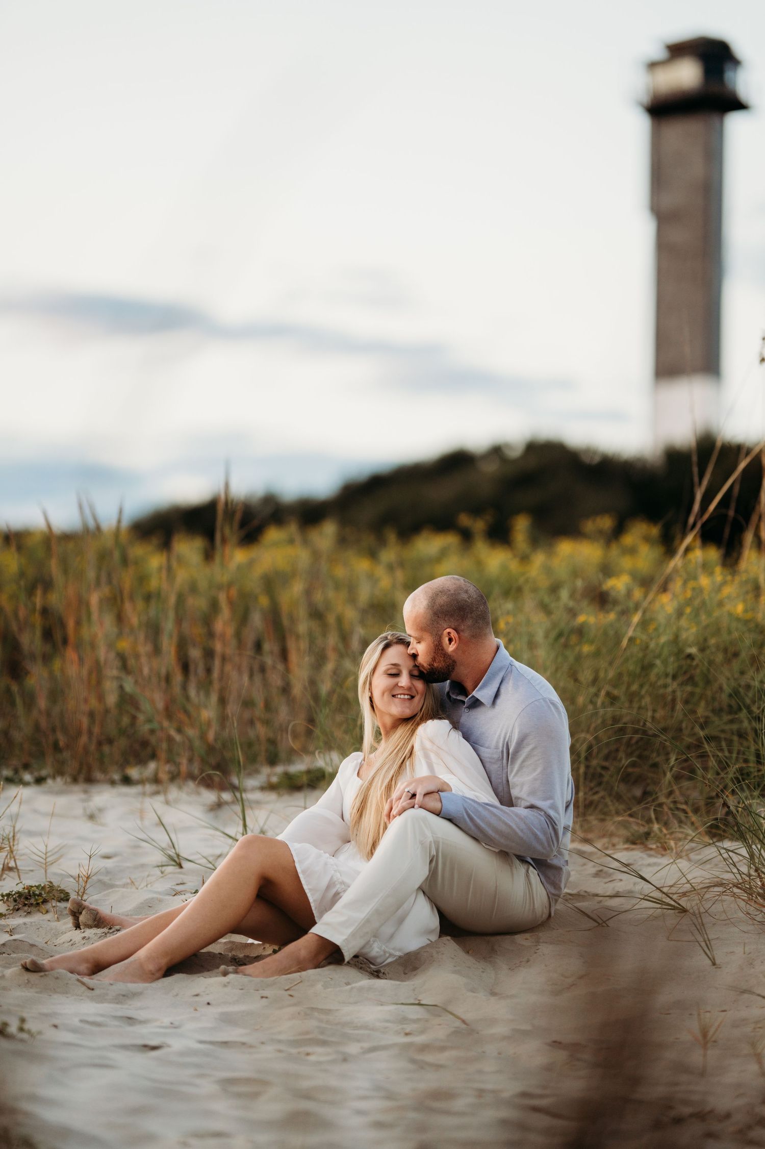 Intimate couple relaxing on sandy beach with lighthouse in background at sunset. Charleston, South Carolina Carolina.