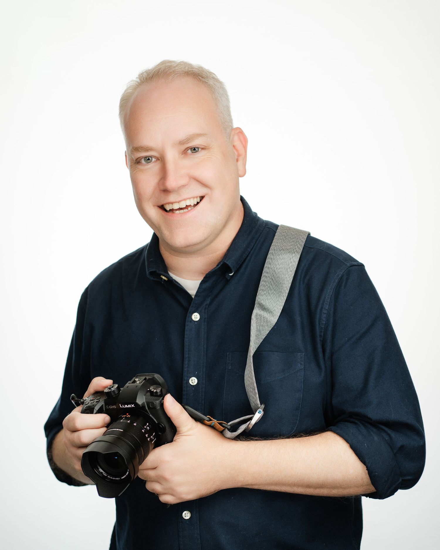 Professional photographer wearing navy shirt holding DSLR camera against white background. Nashville, Tennessee.