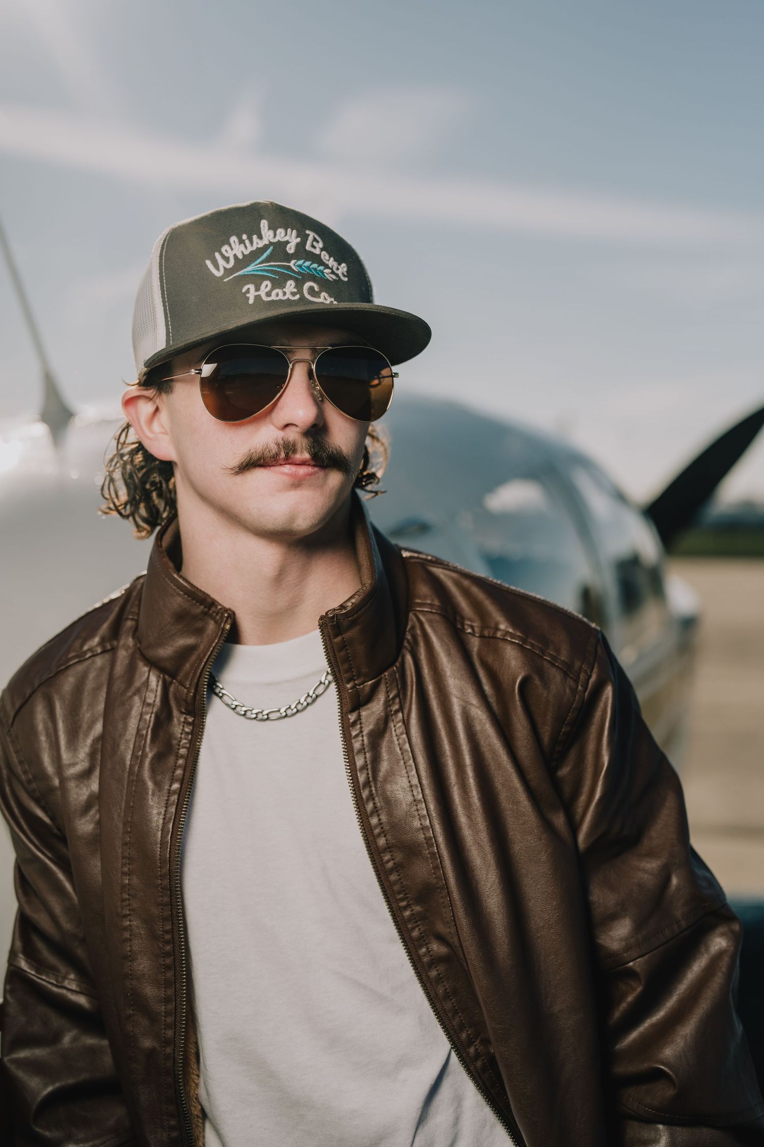 Retro aviator style portrait with leather jacket and trucker cap against airplane background. Nashville, Tennessee.