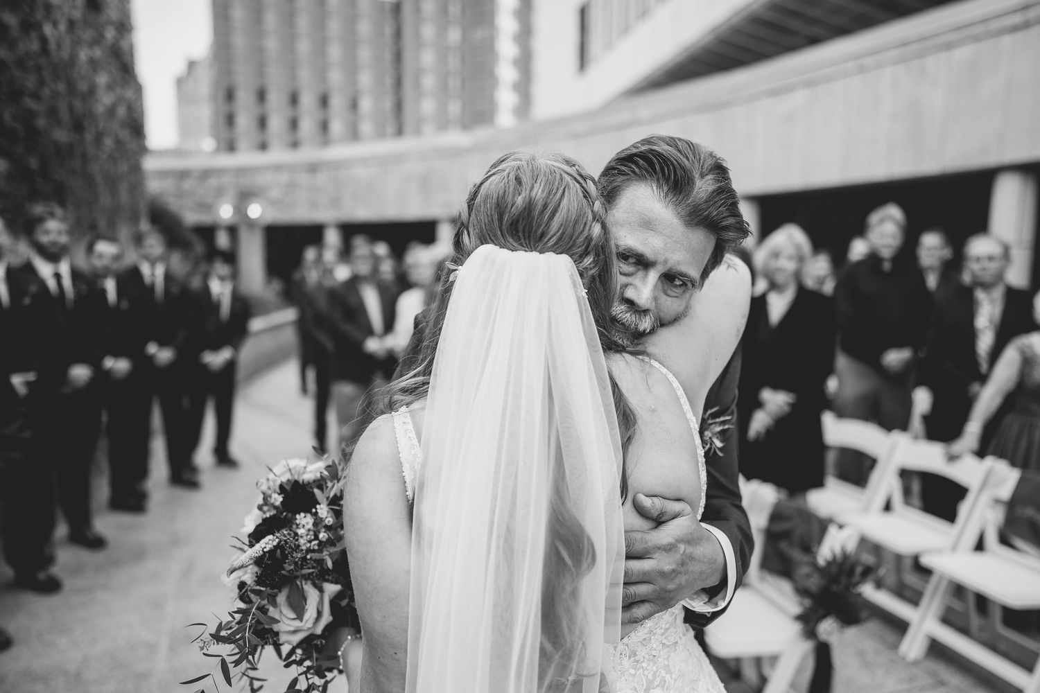 An intimate moment between newlyweds with guests looking on during outdoor ceremony. Milwaukee, Wisconsin.