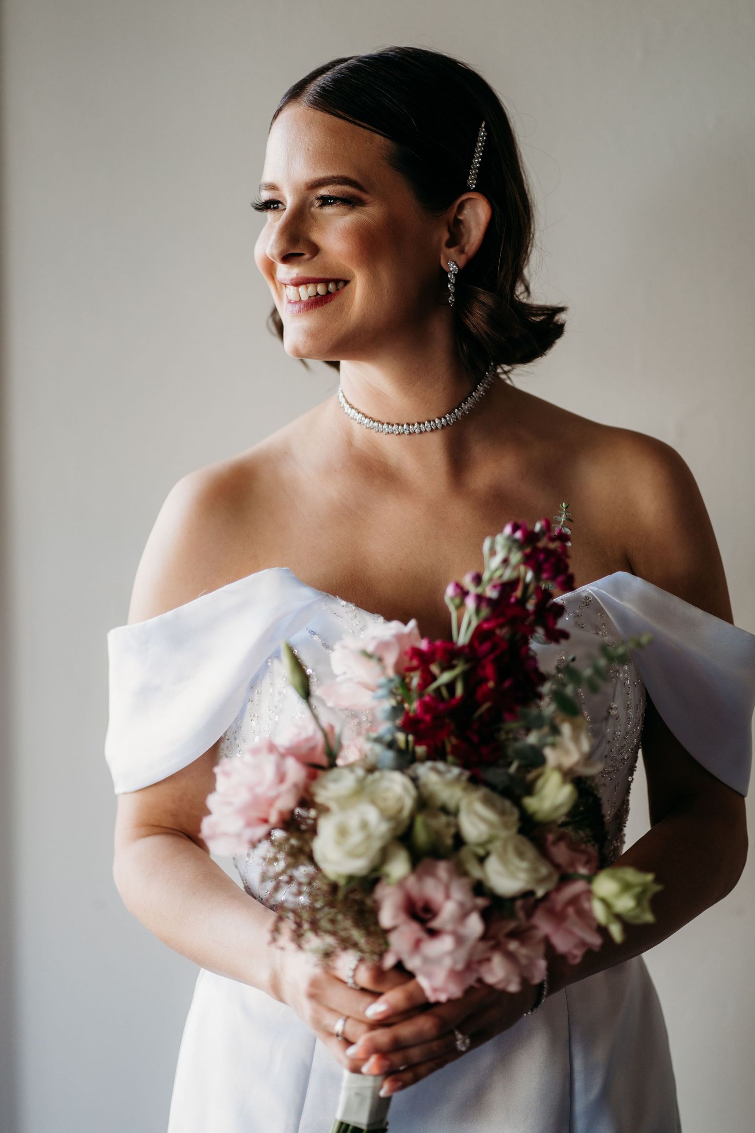 Portrait of someone in an elegant white wedding gown holding a pink and red bouquet. San Francisco, California.