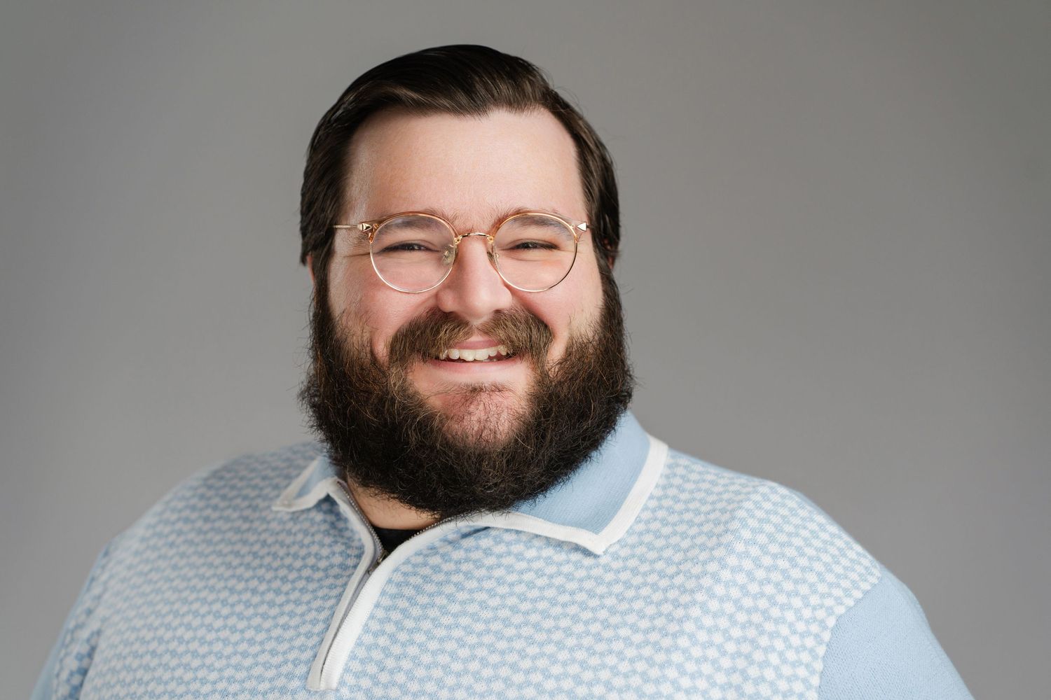 Professional headshot of a bearded person wearing glasses and checkered polo against gray background. Nashville, Tennessee.