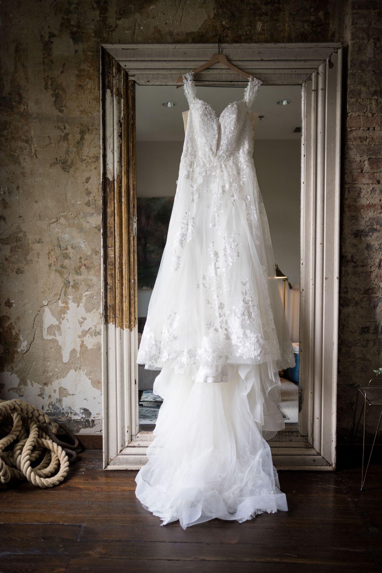 Elegant lace wedding dress hanging on mirror frame in vintage room setting. The Cordelle, Nashville, Tennessee.