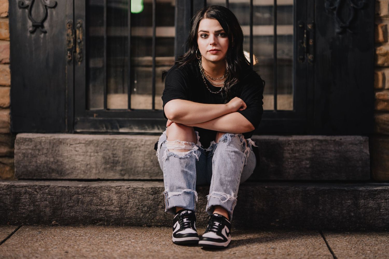 Casual portrait of someone seated on steps wearing ripped jeans, black shirt and sneakers. Nashville, Tennessee.