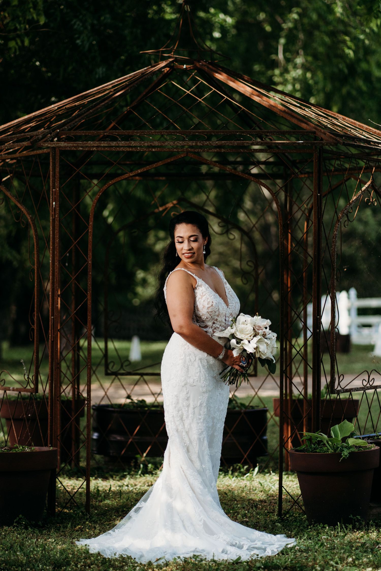 Bride in elegant lace gown poses under rustic garden gazebo with white bouquet. Legacy Farms Nashville, Tennessee.