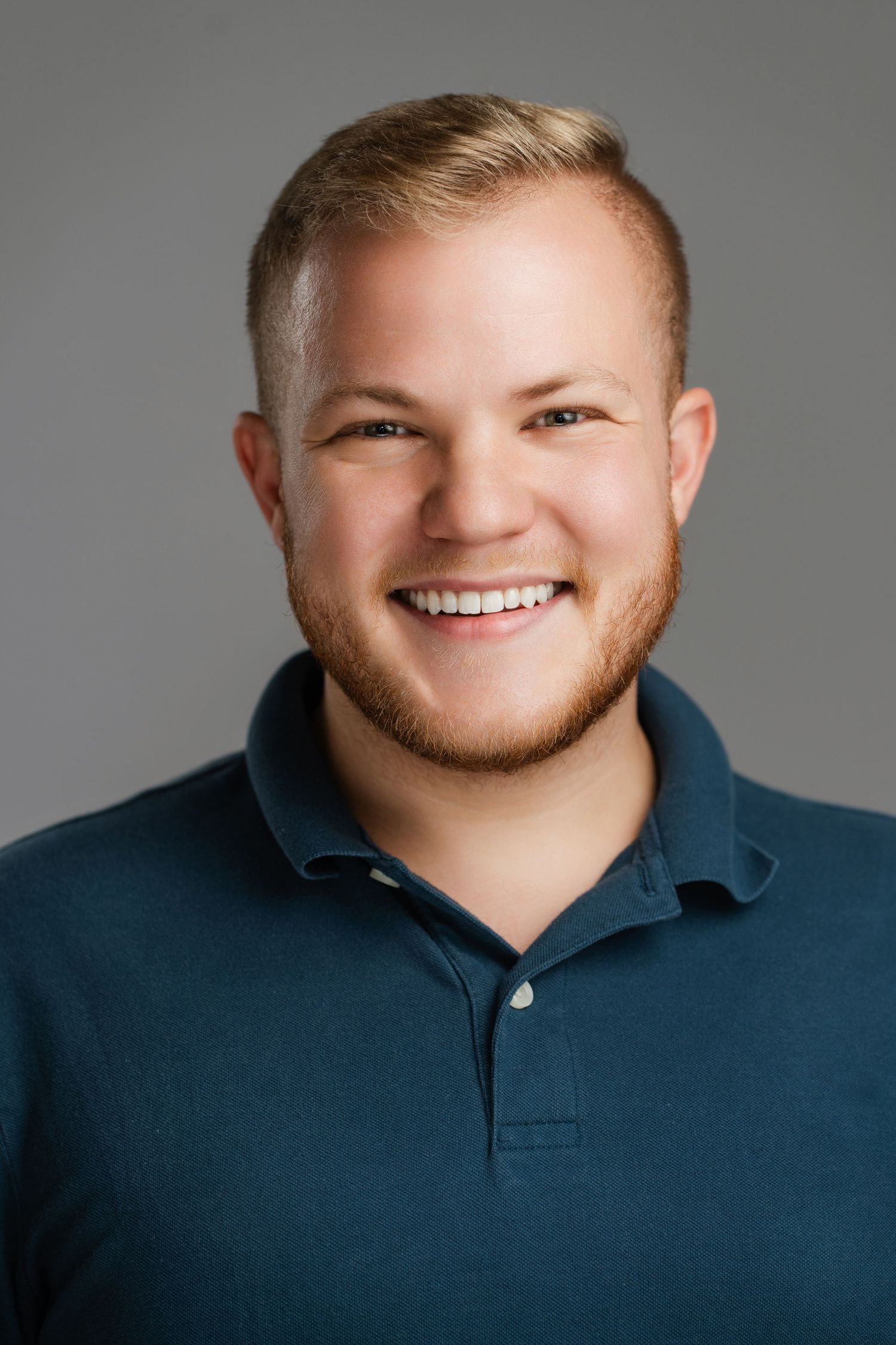 Professional headshot of a person wearing a navy polo shirt against gray background. Nashville, Tennessee.
