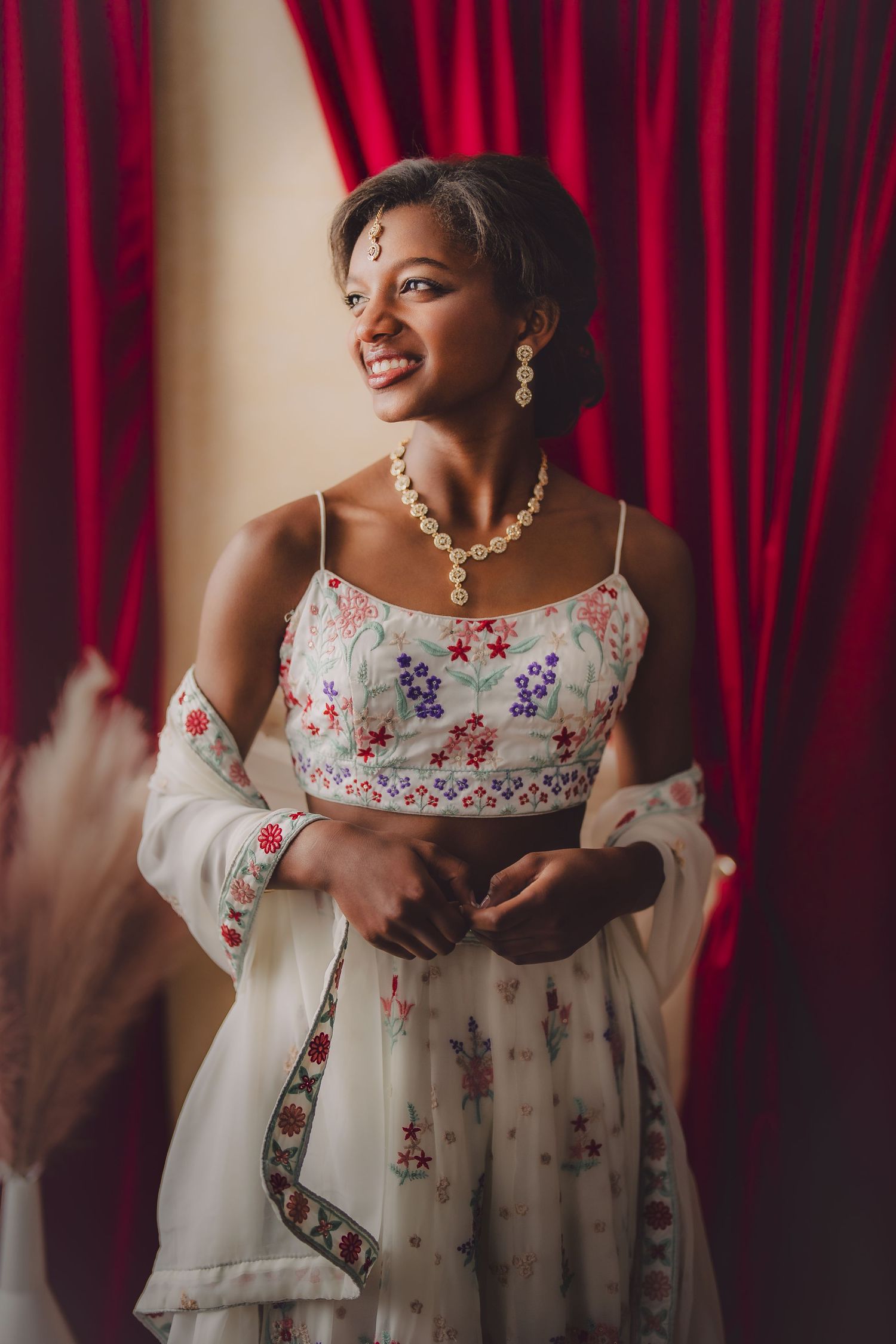 An elegant portrait in front of red curtains featuring a floral dress and pearl jewelry. Murfreesboro, Tennessee.