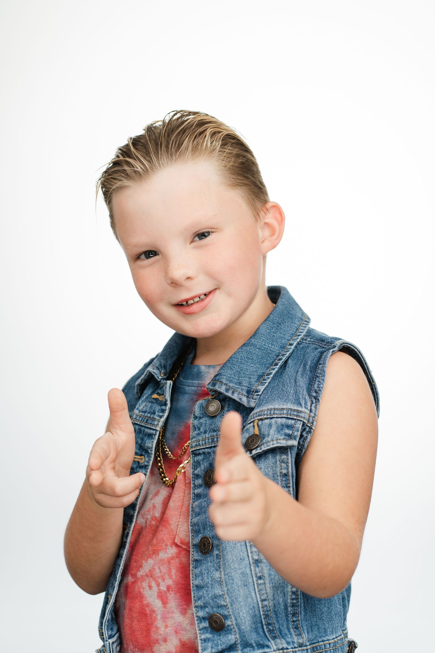 Young person in denim vest giving thumbs up with bright smile against white background.Nashville, Tennessee.