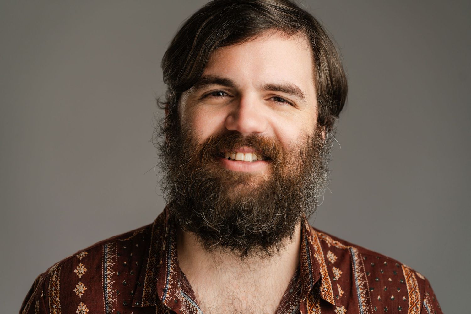 Professional headshot of a bearded person wearing a patterned brown sweater against a gray background. Nashville, Tennessee.