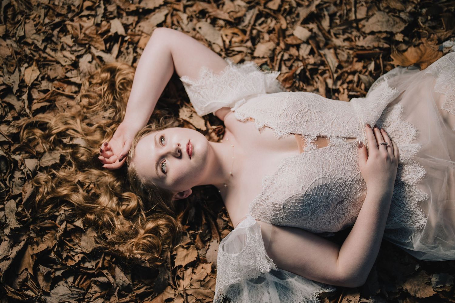 Dreamy autumn fashion photography with model laying in fallen leaves wearing a white lace dress. Nashville, Tennessee.