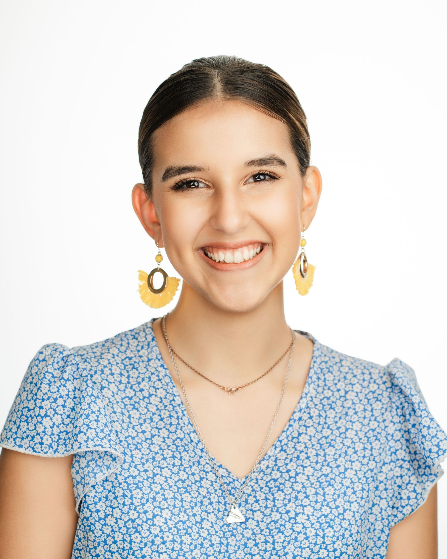 Woman in blue floral dress wearing yellow earrings smiling against white background. Nashville, Tennessee.