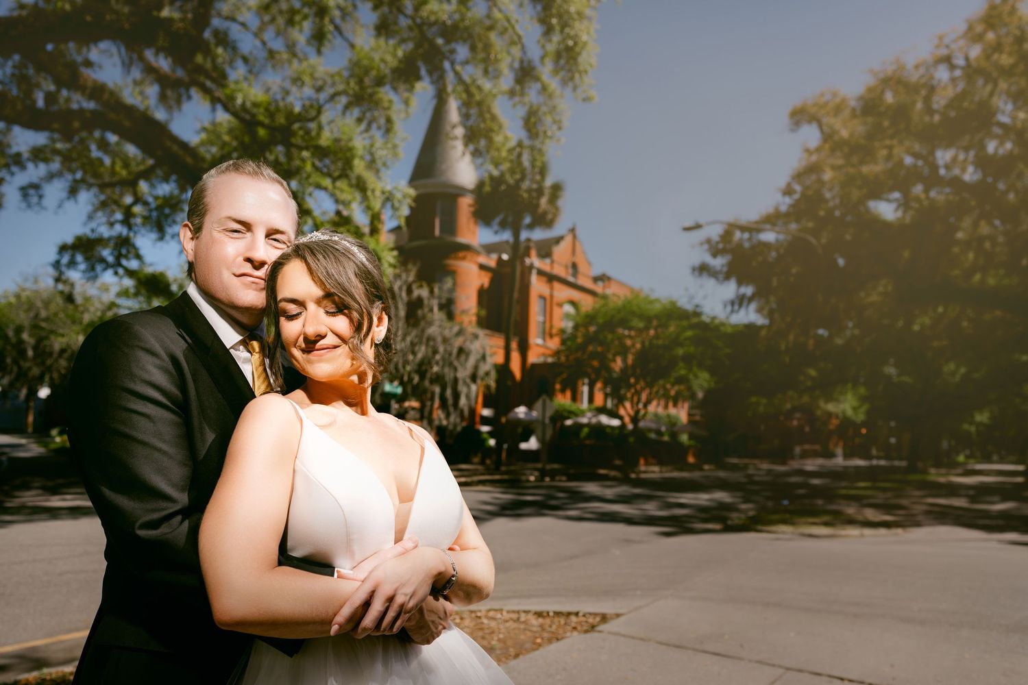 Sunny outdoor wedding portrait of a couple embracing in front of a historic brick church. Savannah, Georgia.