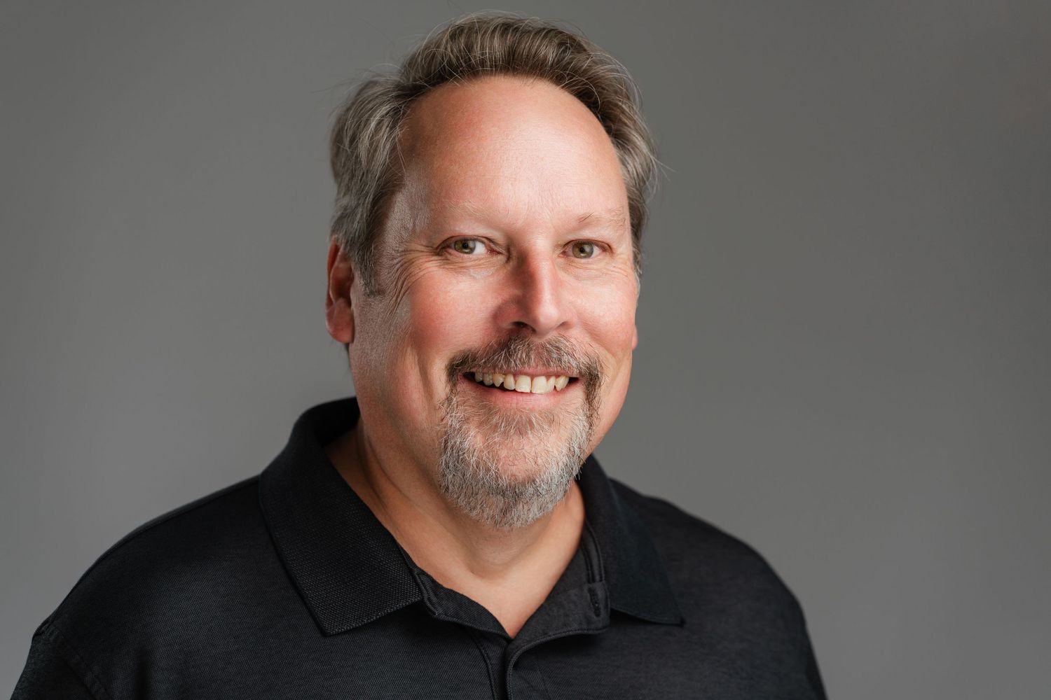 Professional headshot of person in black polo with goatee against gray background. Nashville, Tennessee.