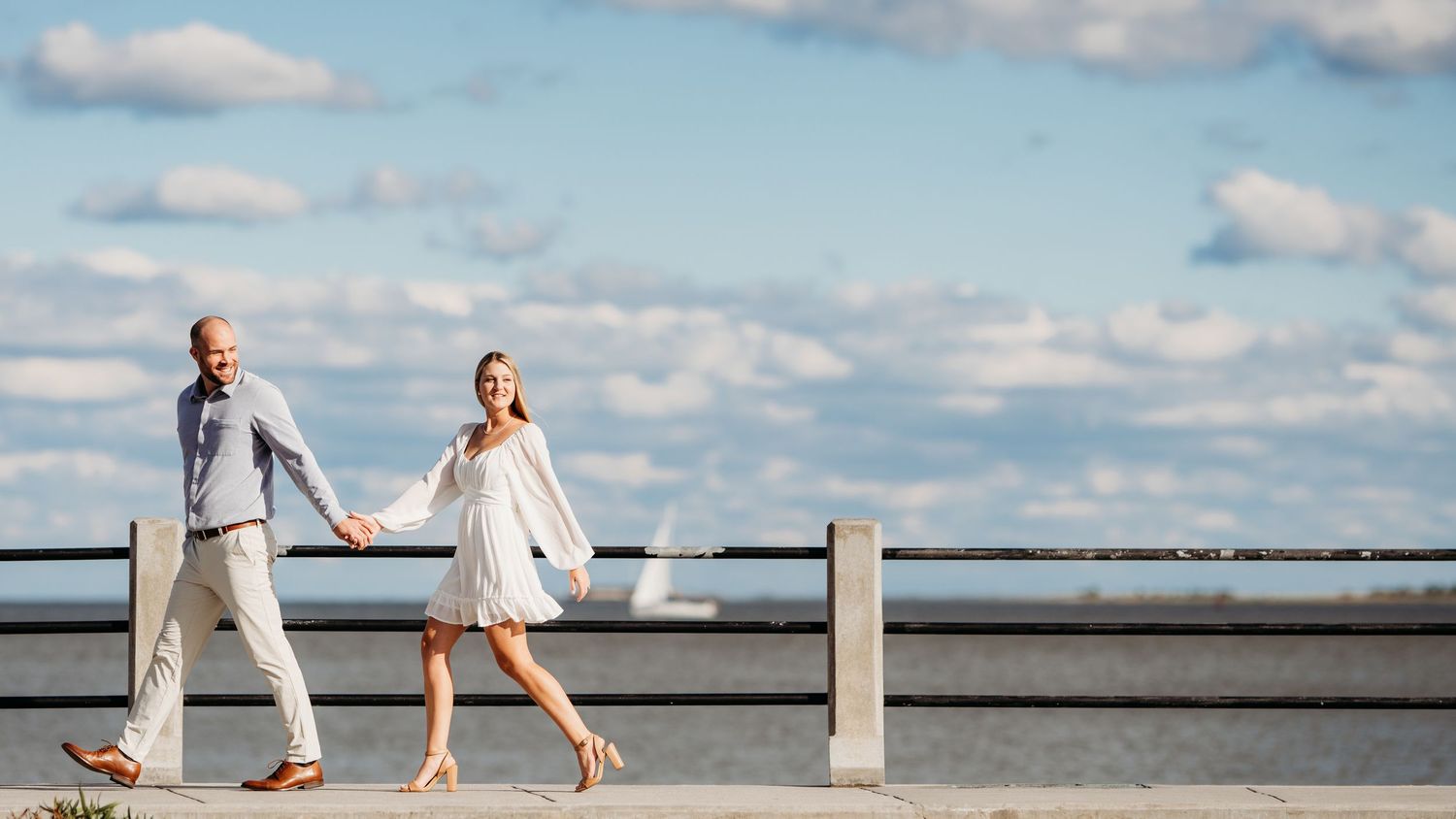 Romantic couple in light clothing walking together on pier under blue summer sky. Charleston, South Carolina.