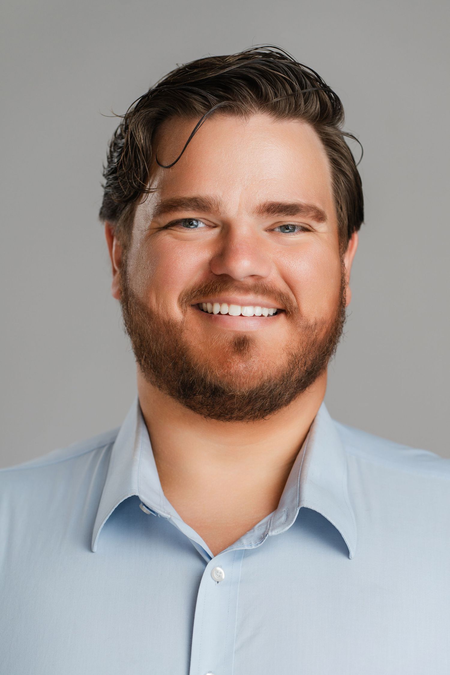 Professional headshot of a person in a light blue button-down shirt smiling against a gray background. Nashville, Tennessee.