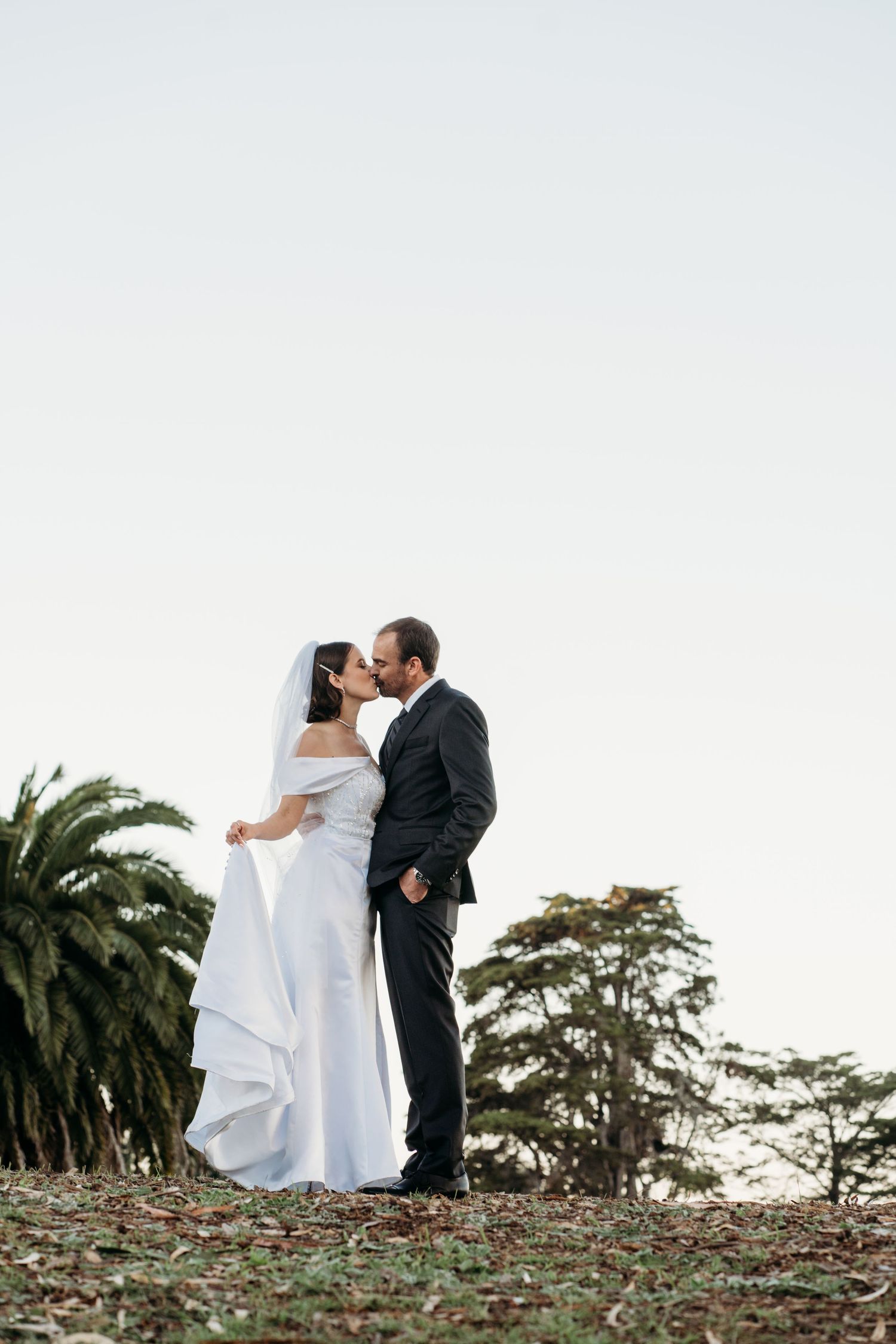 Wedding couple sharing romantic moment on hill with palm trees at sunset. San Francisco, California.