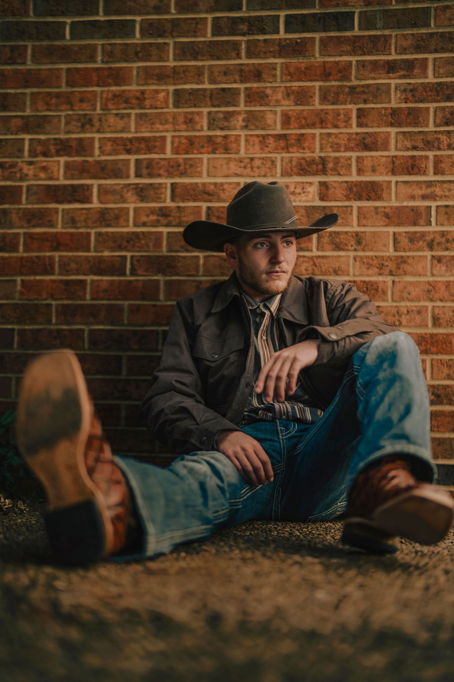 A western-style portrait of someone resting against a brick wall wearing a cowboy hat and boots. Murfreesboro, Tennessee.