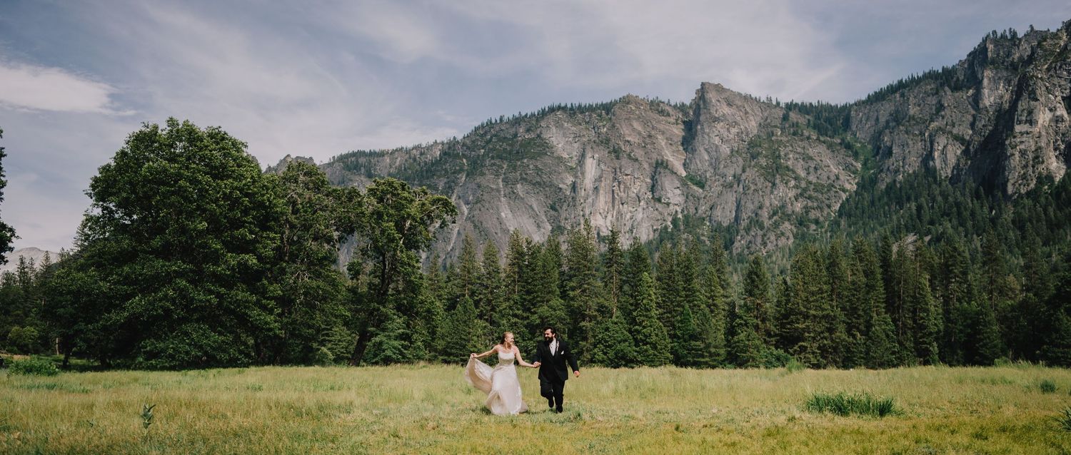 Couple standing in grassy meadow with majestic granite cliffs of Yosemite Valley in background.