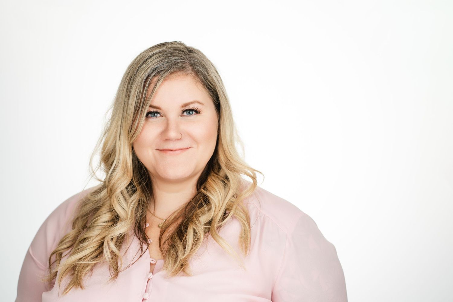 Professional headshot of person in pink top with wavy blonde hair against white background. Nashville, Tennessee.
