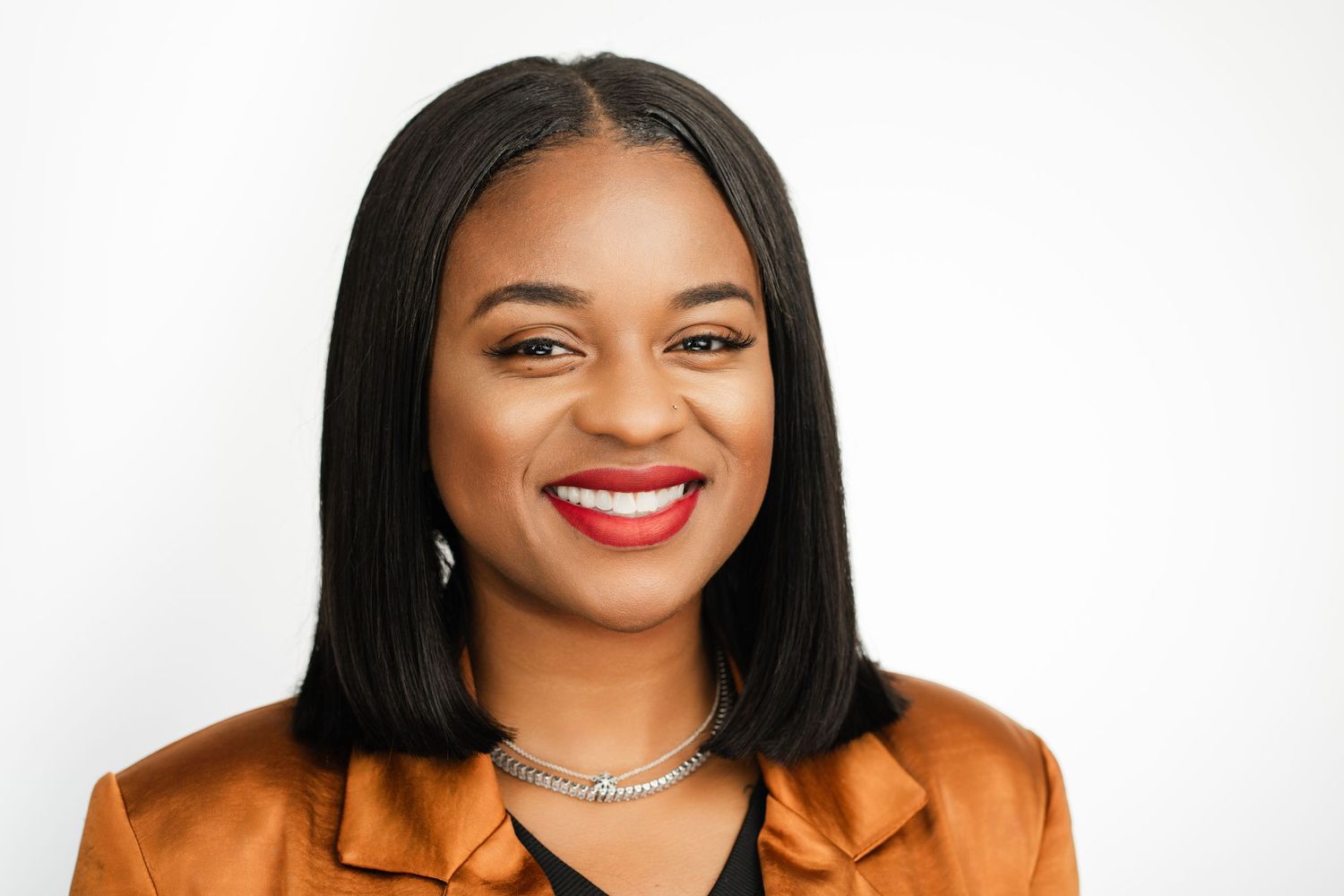 Professional portrait of someone in orange blazer with bright smile against white backdrop. Nashville, Tennessee.
