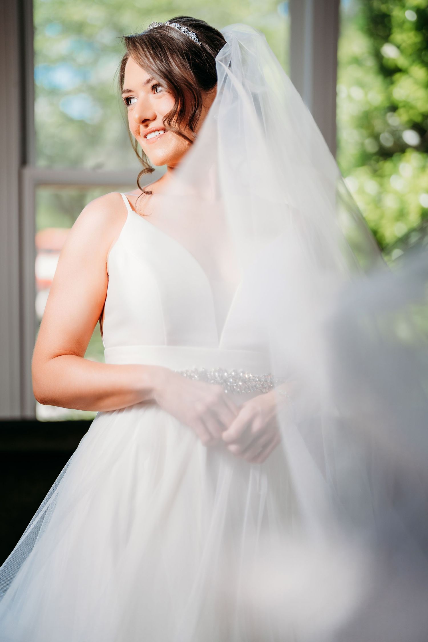 Portrait of a bride in a white wedding dress and veil smiling by a window. Savannah, Georgia.