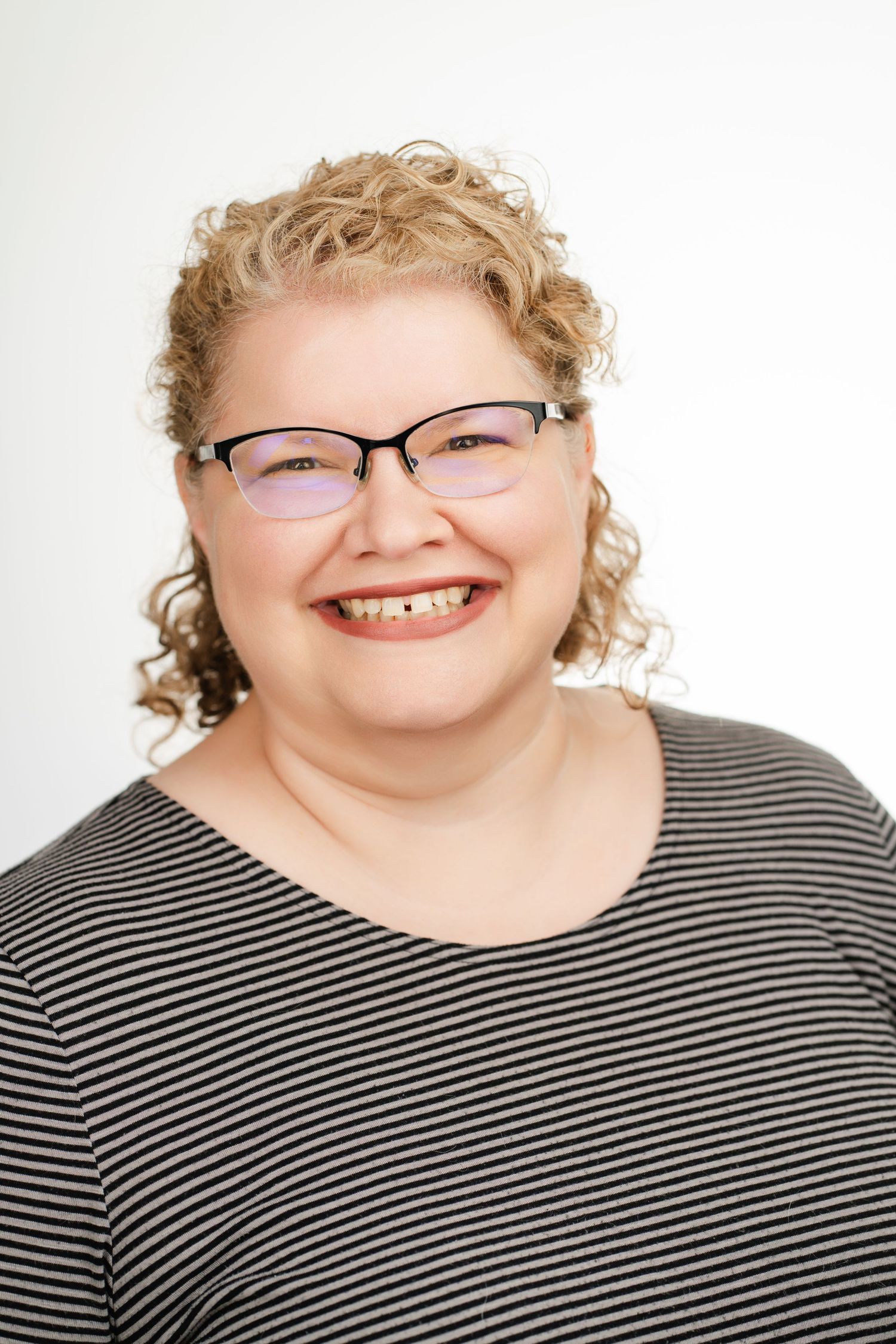 Person with curly hair wearing glasses and striped shirt smiles warmly at camera. Nashville, Tennessee.