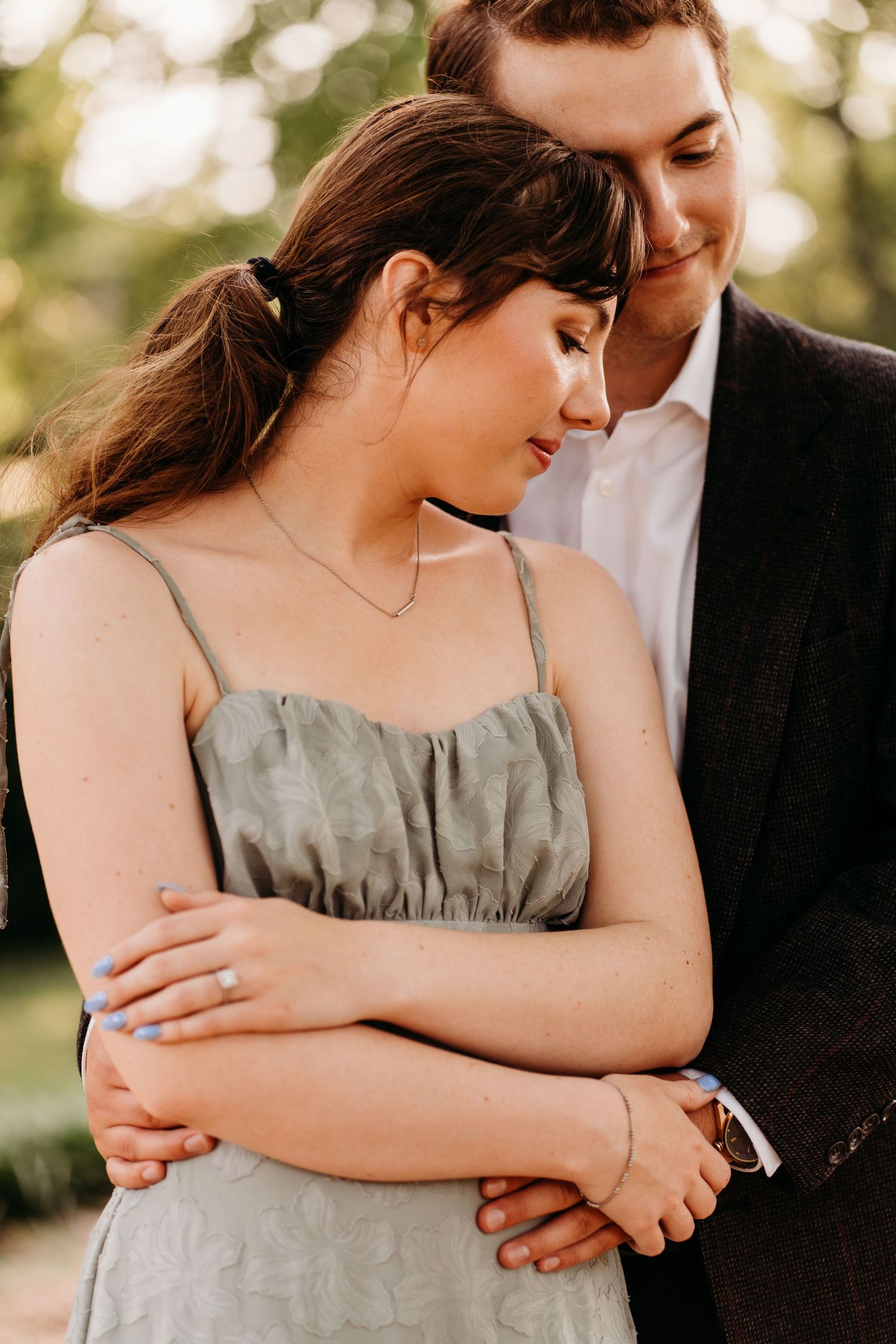 Couple shares intimate moment in soft lighting as he embraces her from behind while she wears a gray dress. Nashville, Tennessee.