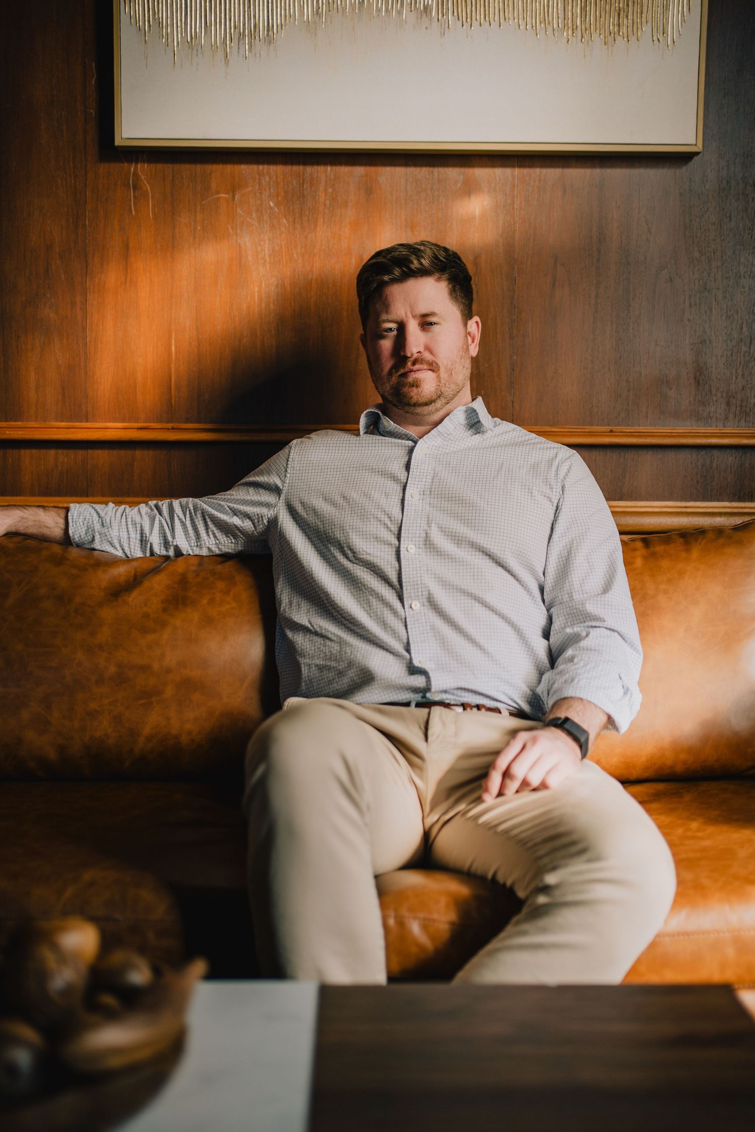 Person in light colored shirt relaxing on brown leather couch with artwork behind. Nashville, Tennessee.