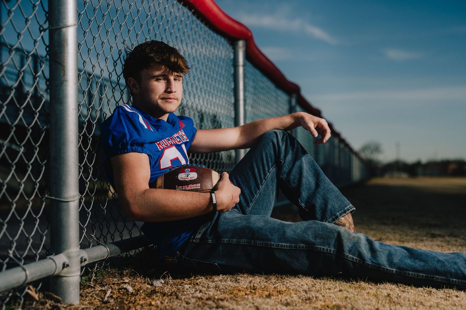 A casual portrait of someone in sports attire resting against a chain-link fence. Murfreesboro, Tennessee.