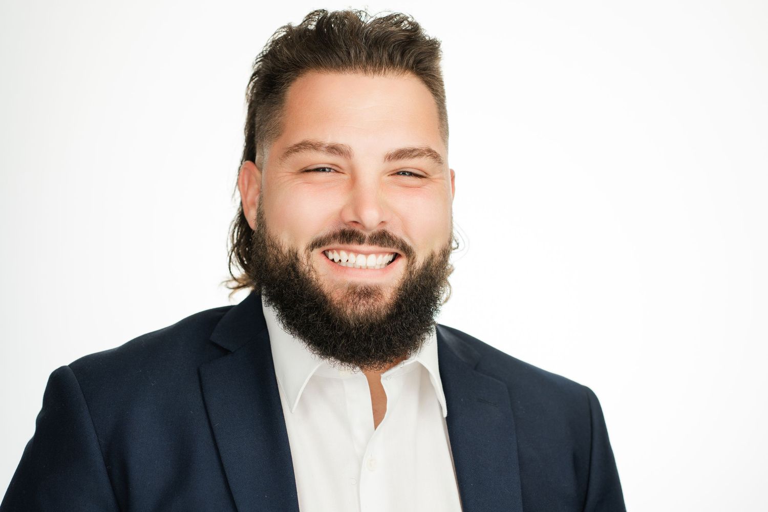 A bearded man in a navy blazer and white shirt smiles broadly at the camera. Nashville, Tennessee.