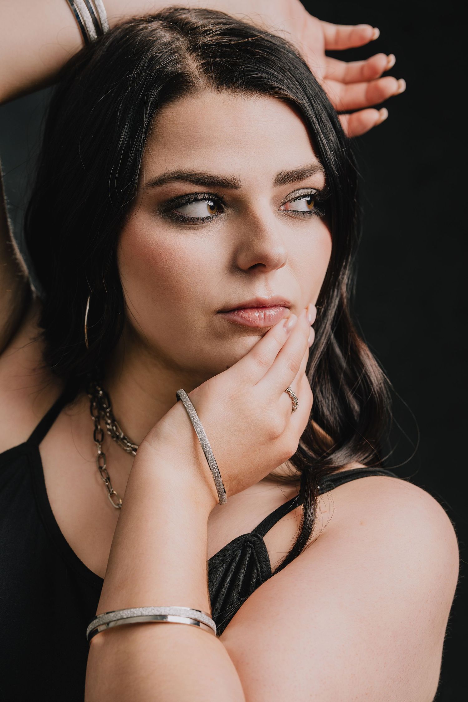Dark-haired model with dramatic portrait lighting poses thoughtfully against black background wearing silver jewelry. Nashville, Tennessee.