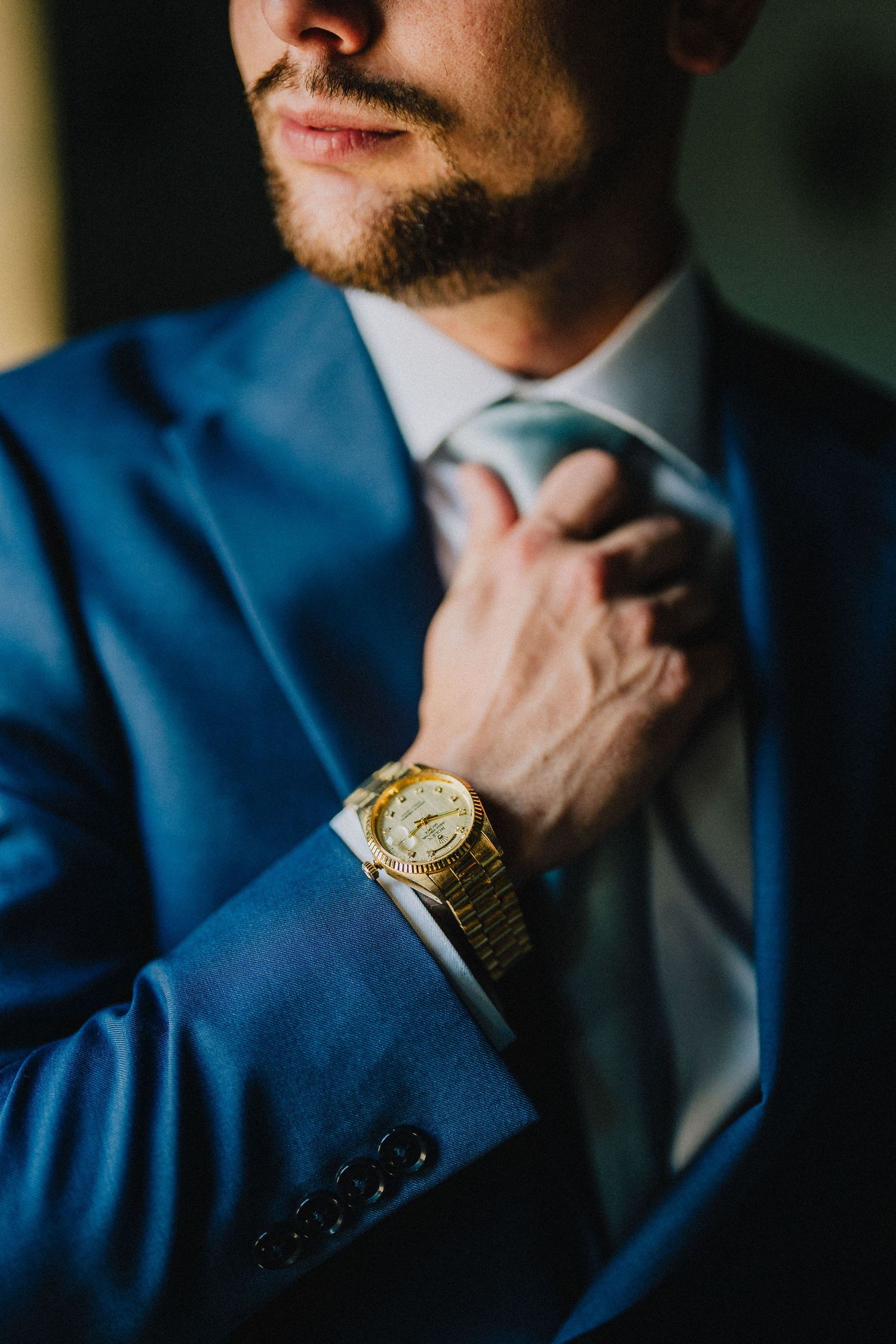Close-up of a person in a navy blue suit adjusting their tie while wearing a gold watch. Nashville, Tennessee.