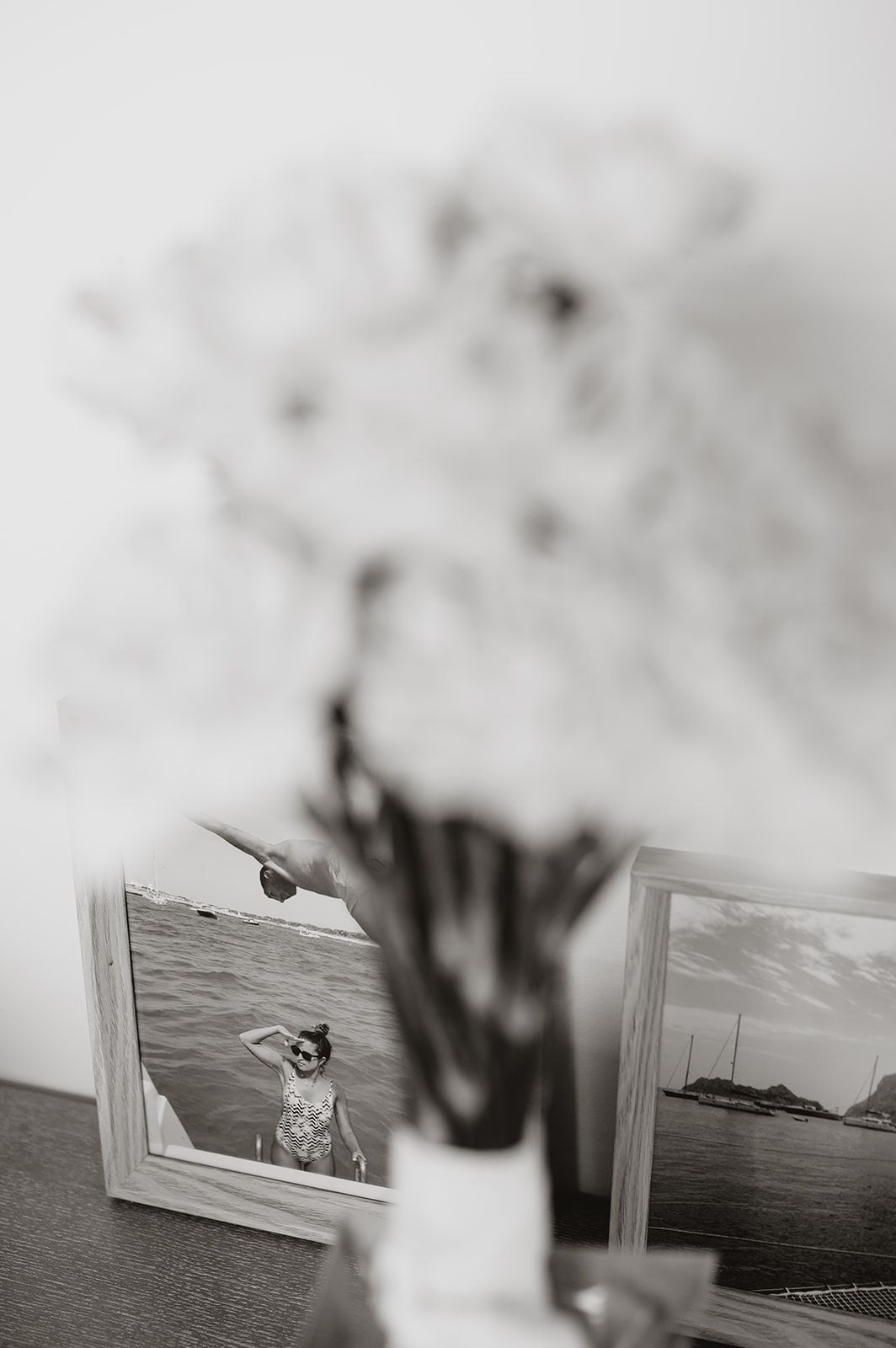 Black and white photo showing framed photographs next to a vase with flowers on a surface.