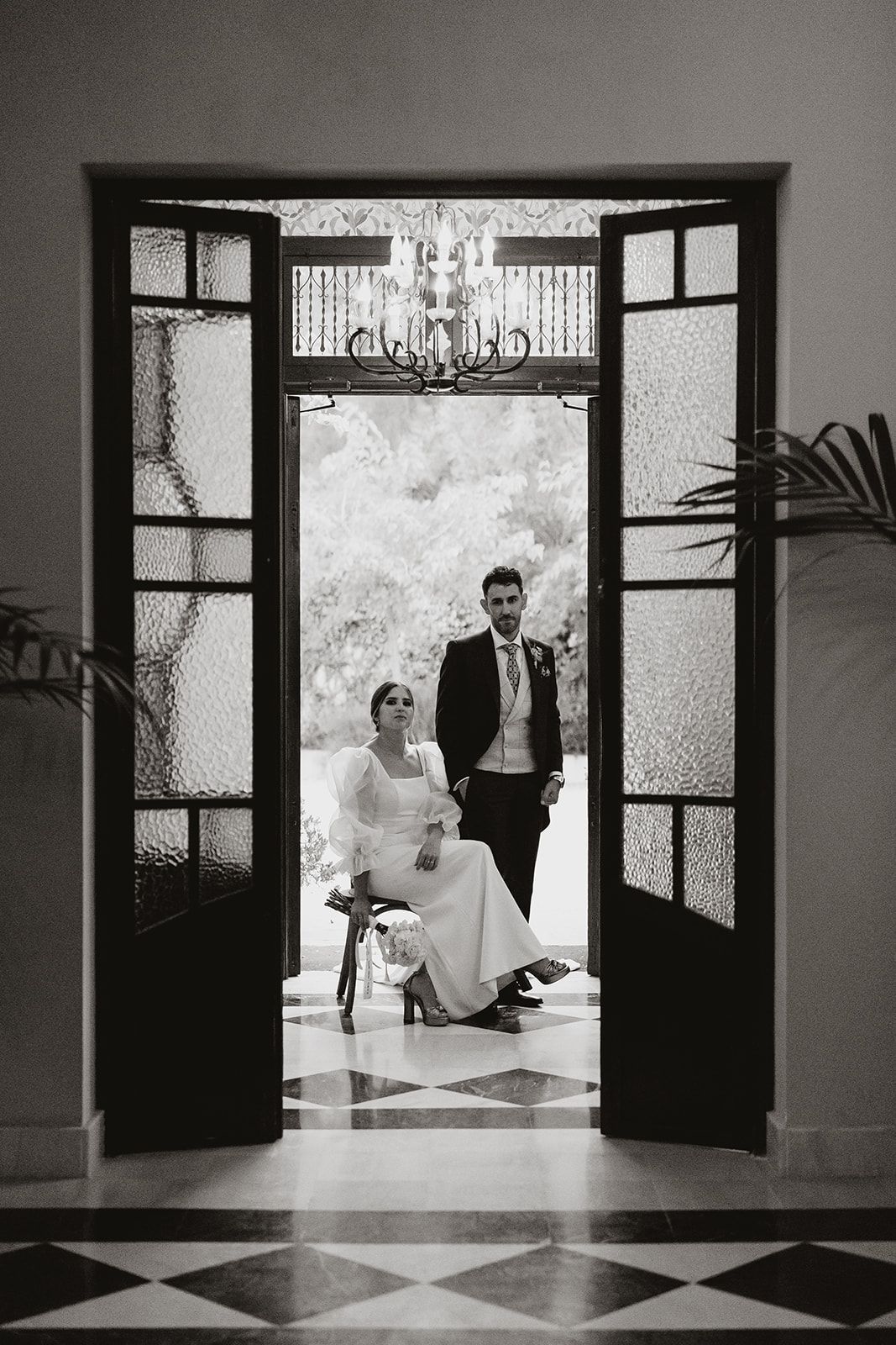 Elegant black and white doorway frame of couple posing beneath crystal chandelier.