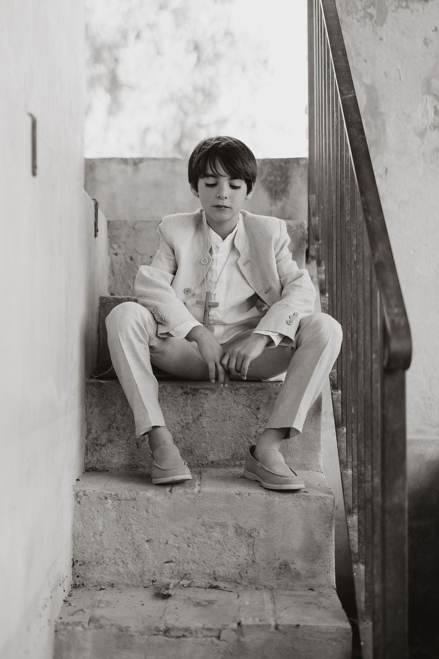 Black and white portrait photograph of a person in a light colored suit sitting on concrete stairs.