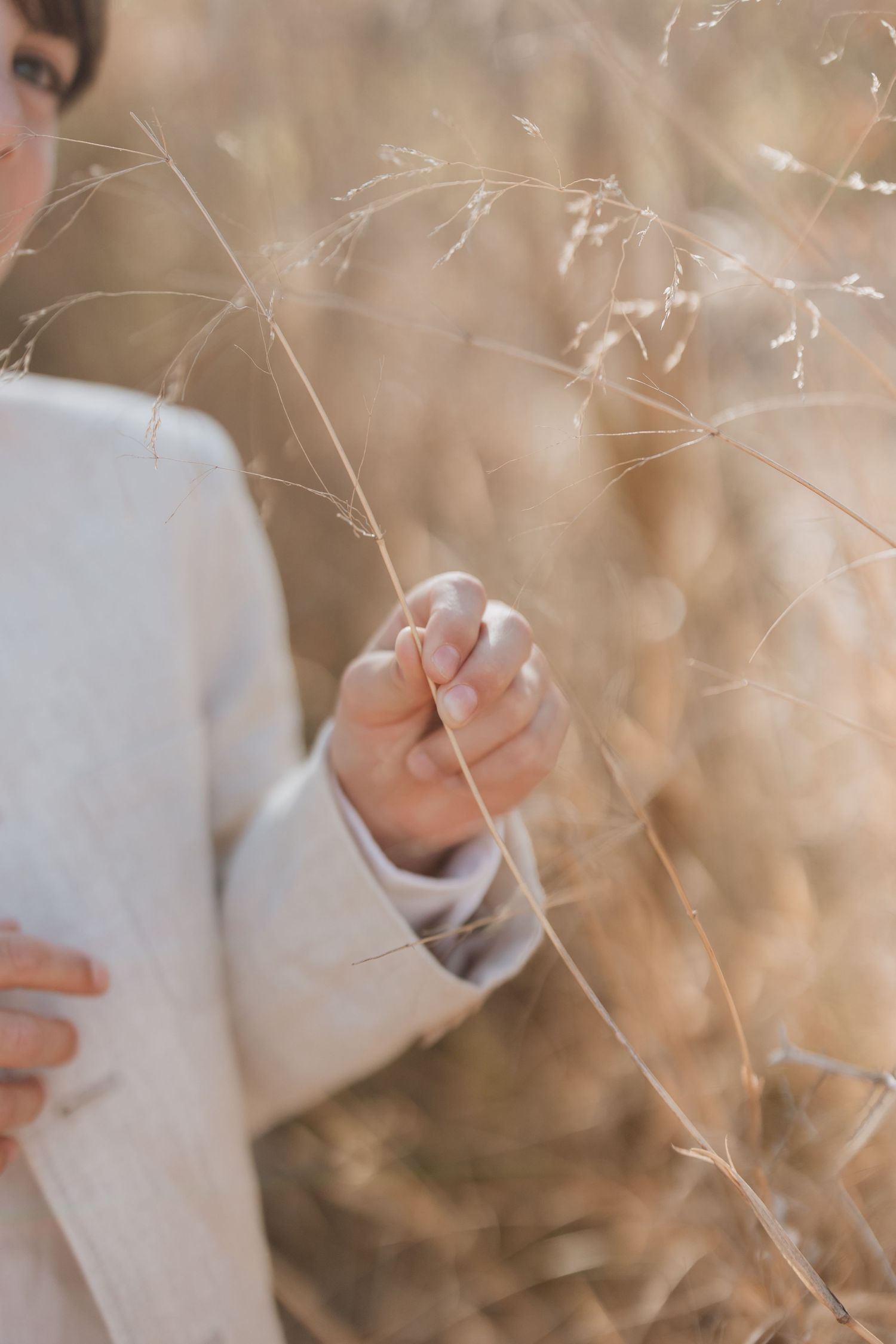 Close-up view of delicate fingers gently holding dried grass stems against a soft bokeh background.