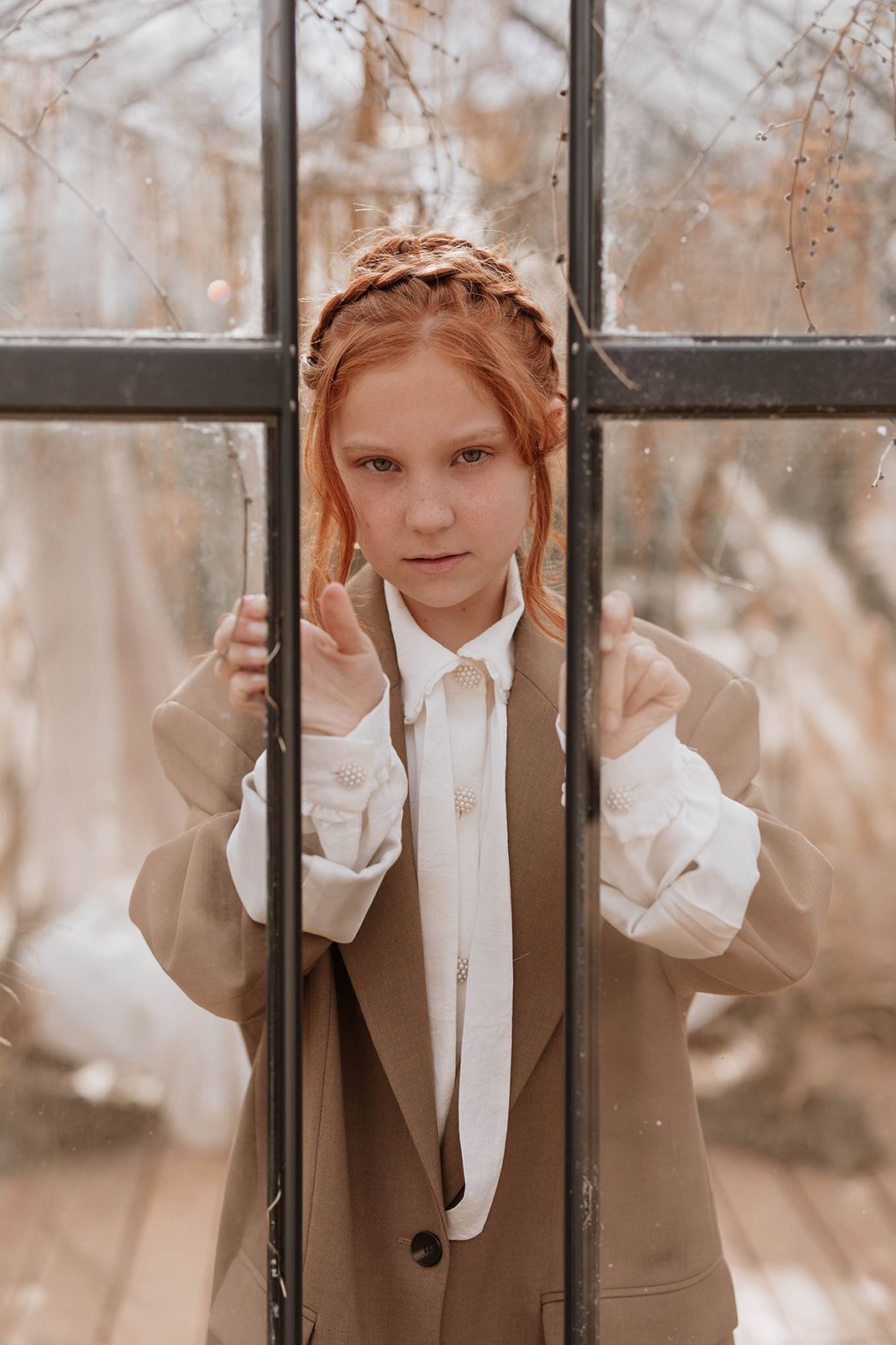 A vintage-inspired portrait through greenhouse windows with elegant styling and neutral tones.