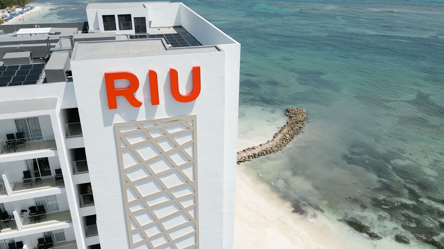 RIU hotel logo on white building exterior with turquoise ocean and beach view.