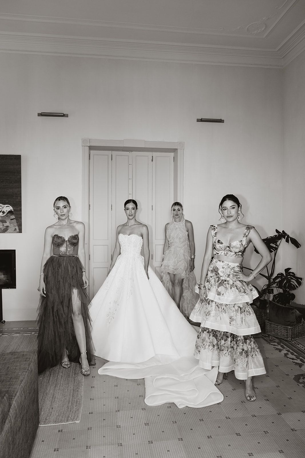 Black and white photo of wedding party posing in varied length dresses against white walls.