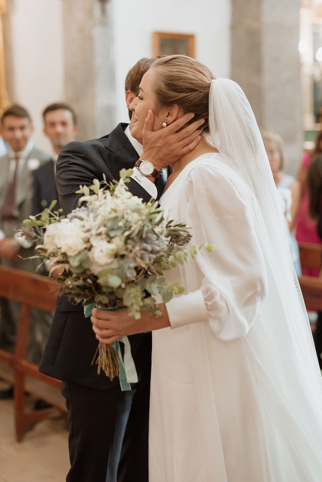 Emotional wedding moment with bride holding white and green bouquet in church.