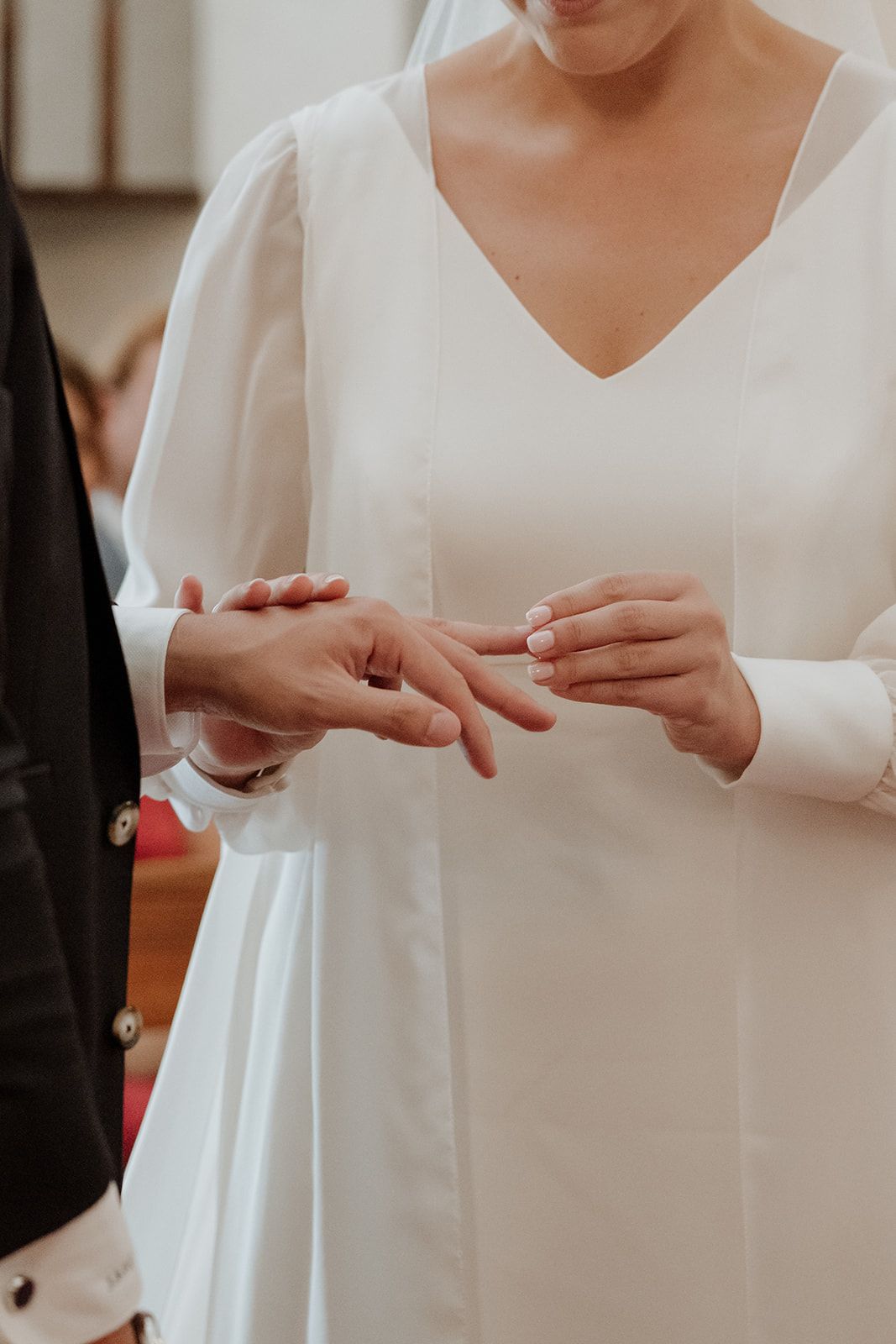 Close-up of hands exchanging wedding rings during a ceremony with white bridal gown sleeves visible.