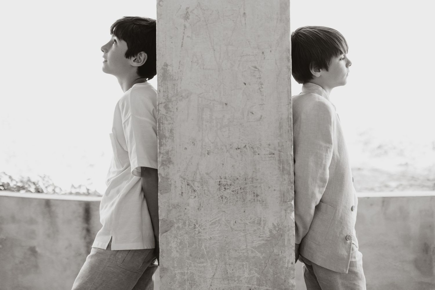 Two figures in white outfits standing on opposite sides of a concrete pillar in black and white.