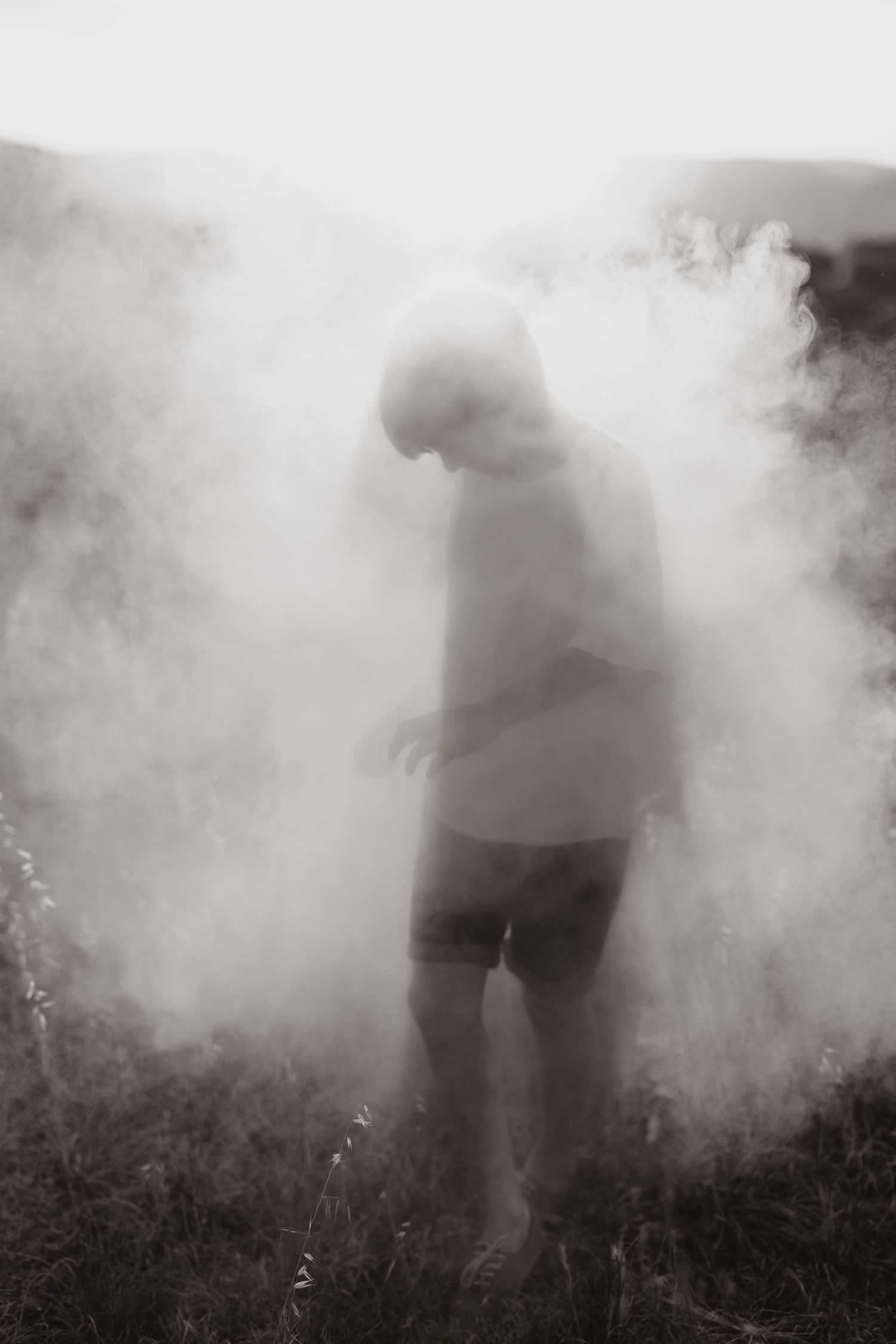 A mysterious silhouette emerges through thick white smoke against a dark background in an artistic monochrome photograph.